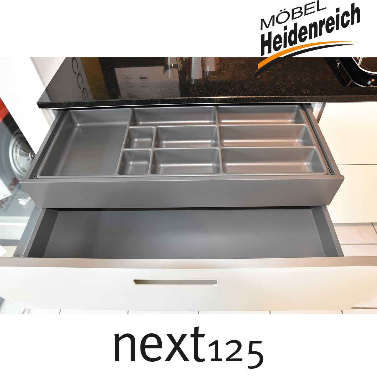 Geöffnete Schublade mit Besteckeinsatz aus grauem Plastik.