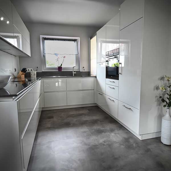 Küche Familie Obermüller U-förmige weiße Hochglanz-Küche mit schwarzer Arbeitsplatte und vielen Ober- und Unterschränken.