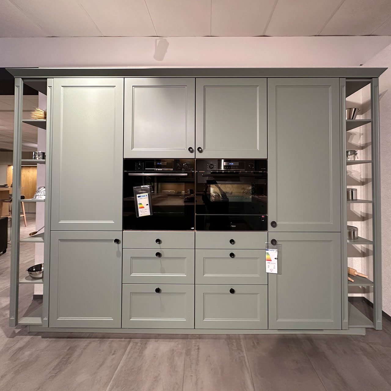 Diese Küchenzeile ist links und rechts mit offenen Regalen abgeschlossen. Hier verbergen sich Großelektrogeräte und viel Stauraum.