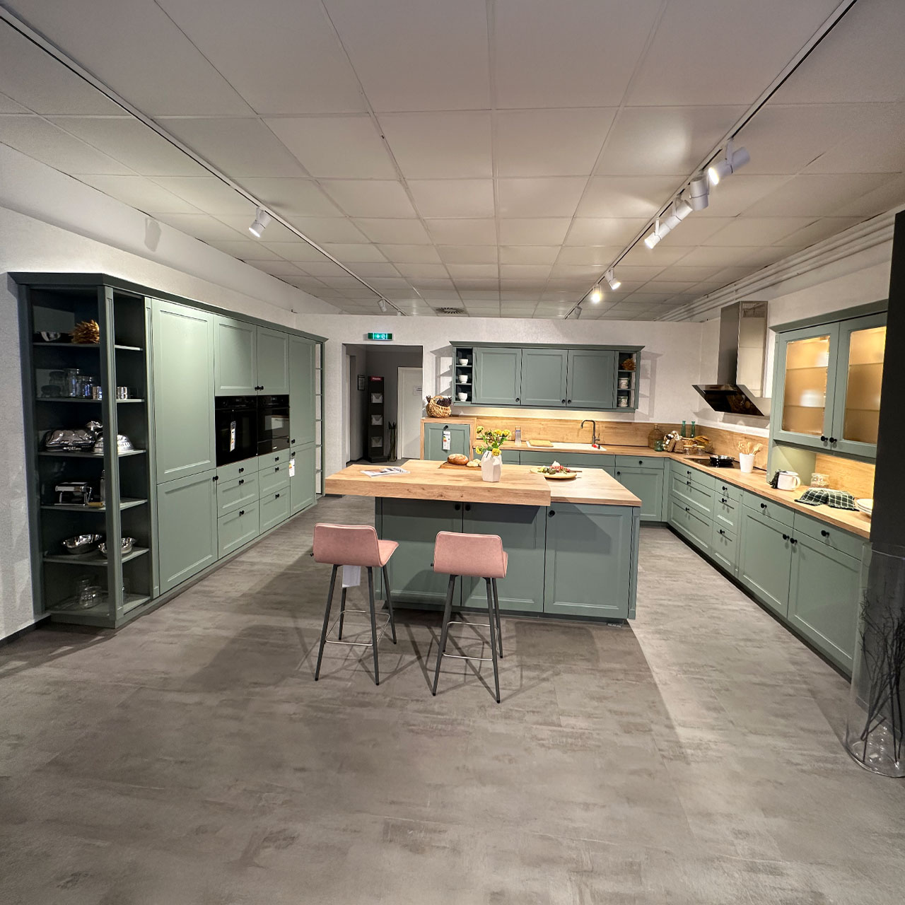 Großzügige grüne Landhausküche mit Kochinsel, Holzarbeitsplatte und Holz-Theke mit viel Stauraum.