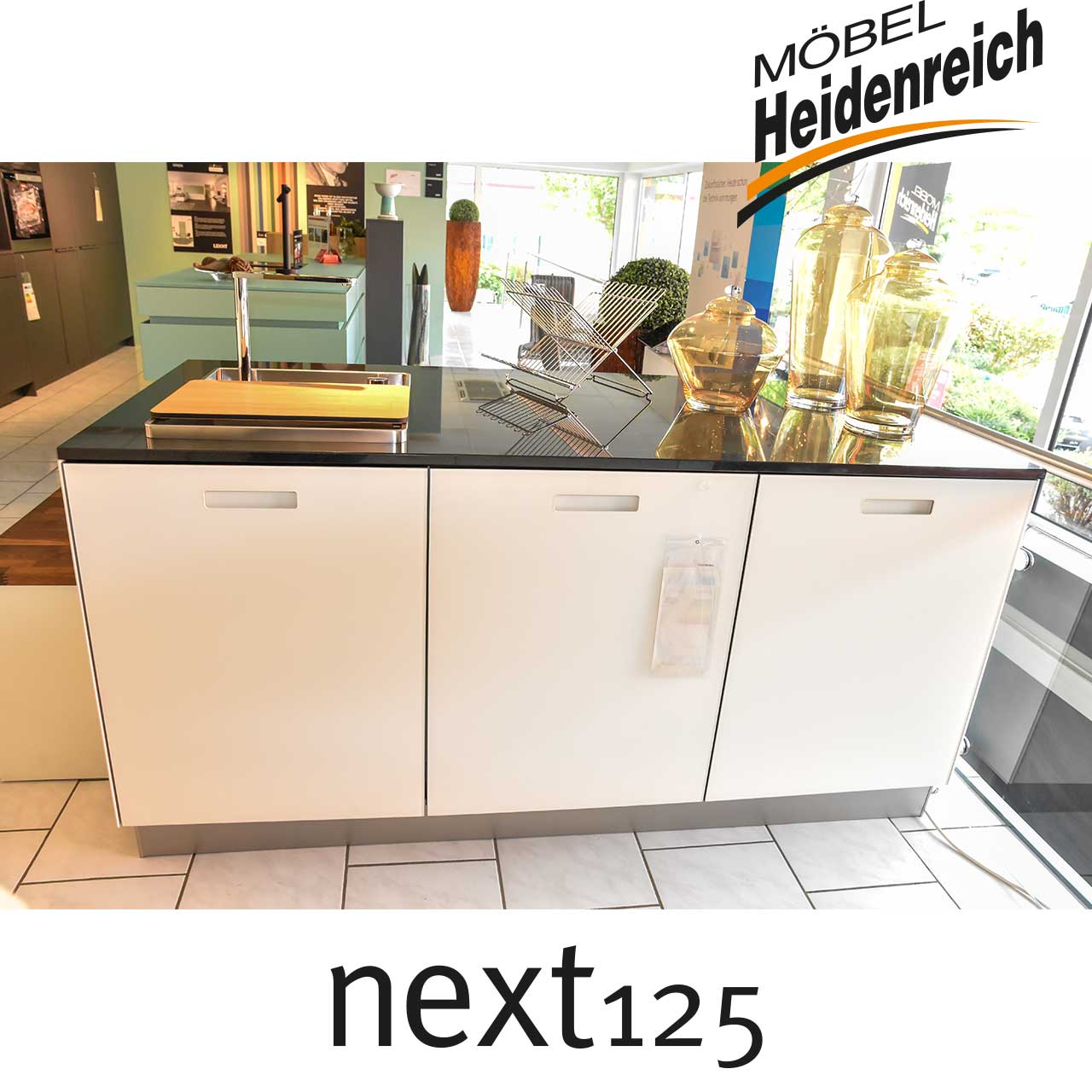 Weiße Kücheninsel mit glänzend schwarzer Abdeckplatte, in welche die Spüle eingelassen ist.