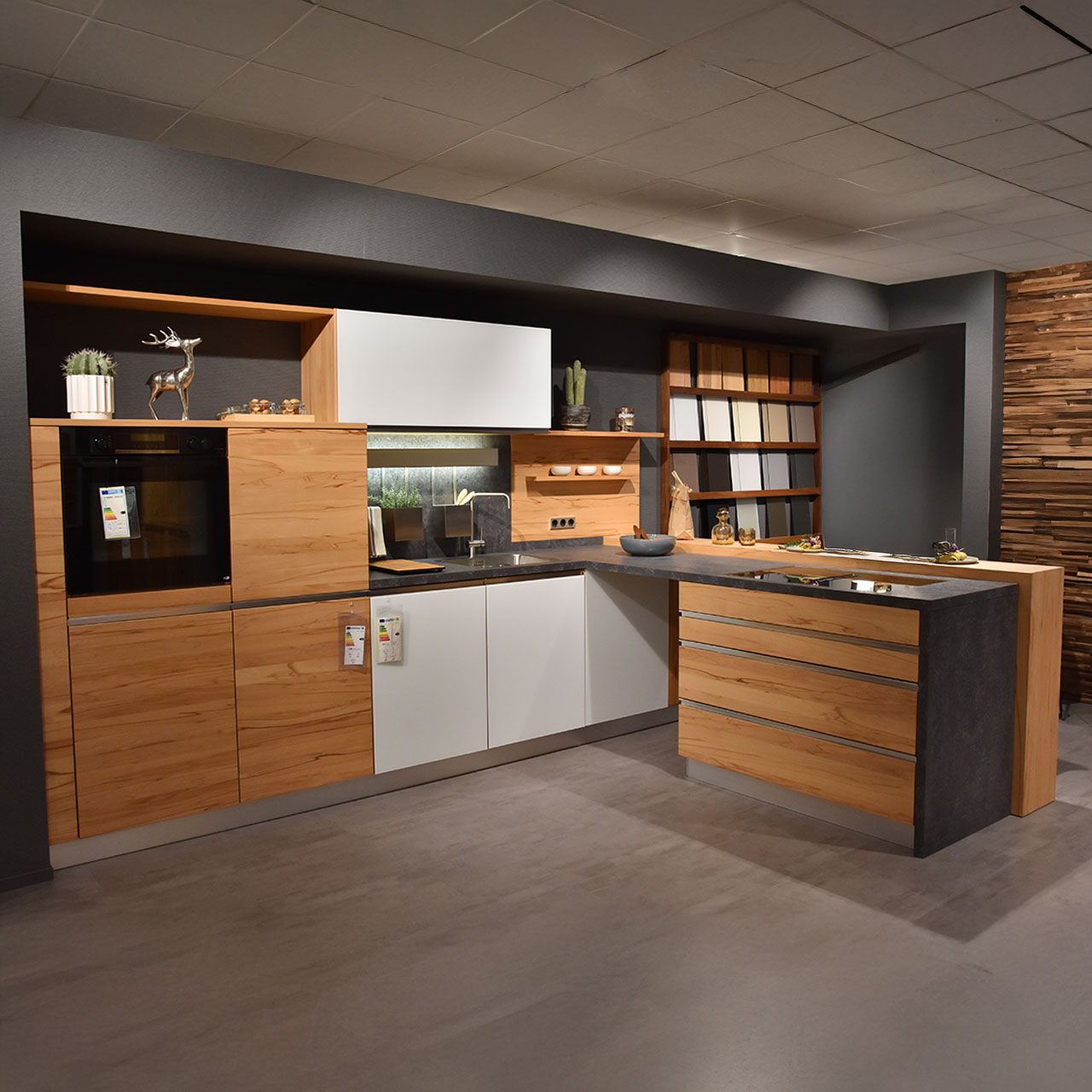 Küche in dunklem Holz mit Schränken links, teilweise mit weißen Türen kombiniert, und Theke mit Edelstahlspüle rechts.