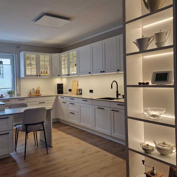 Küche Familie Stumpf Helle Küche im Landhausstil mit Kassettentüren als Eckküche mit beleuchtetem Regal rechts.