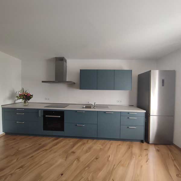 Küche Familie Salhaoui Petrol-farbene Küchenzeile mit Griffen und Stand-by-Kühlschrank.