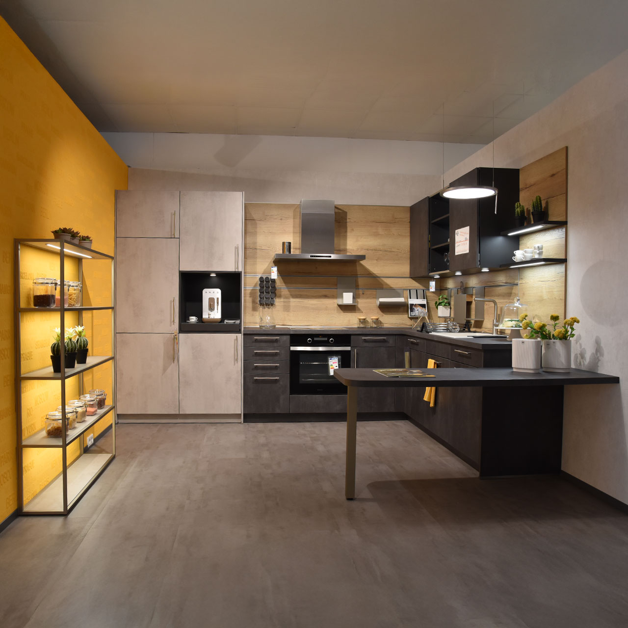 Einbauküche mit beleuchtetem Regal links, in der Mitte und rechts Küchenzeilen, im Vordergrund integrierter Essplatz.